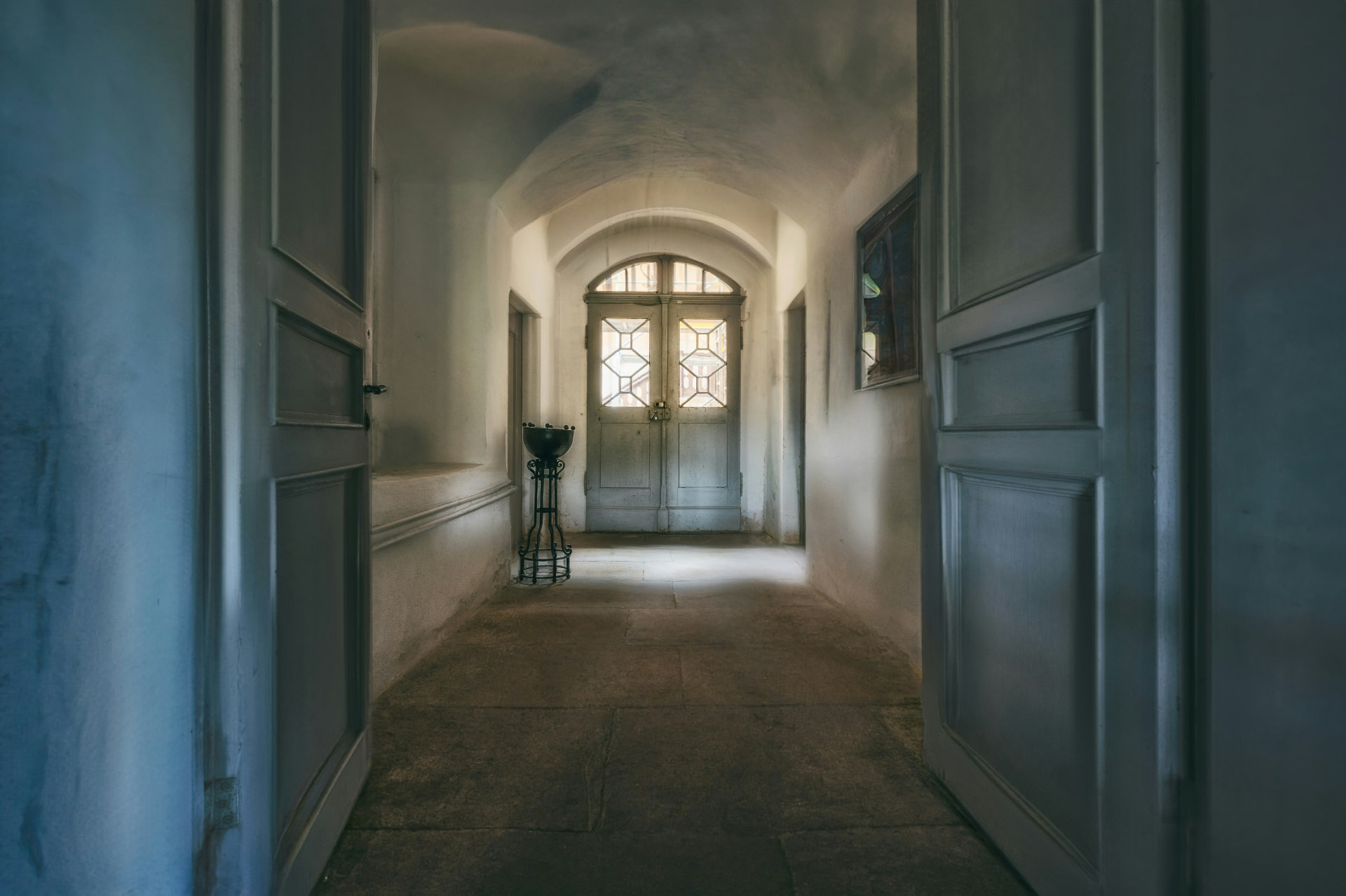 An arched door at the end of a softly lit hallway, light coming through its windowpanes